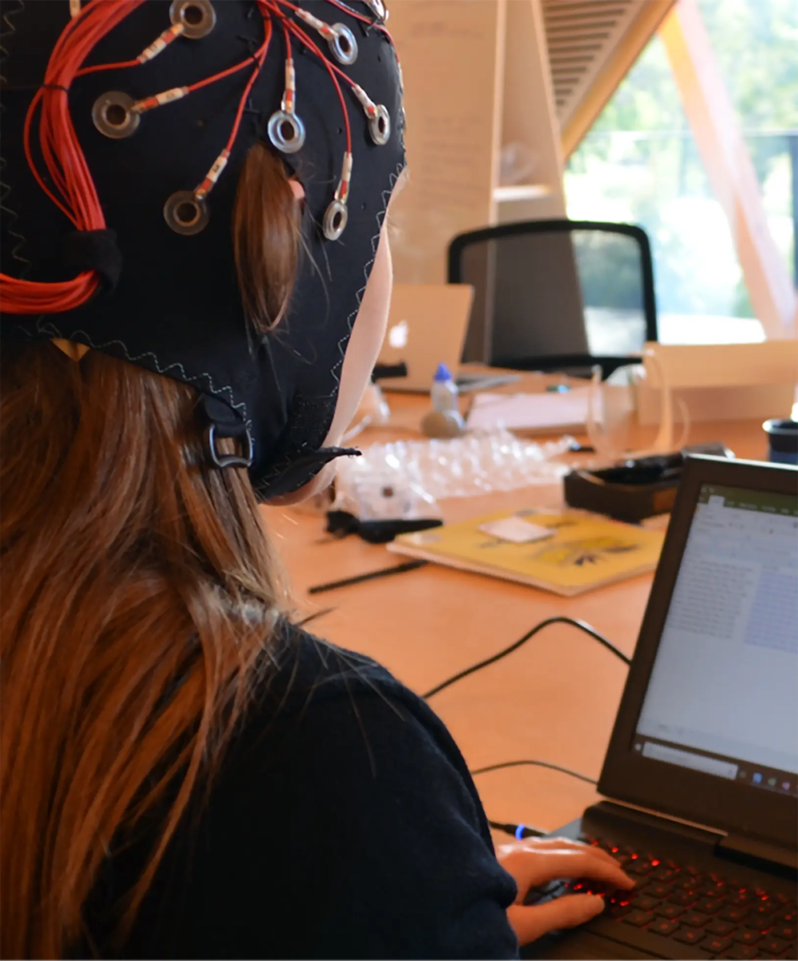 Woman wearing an Emotiv Epoc Flex in front of an open laptop