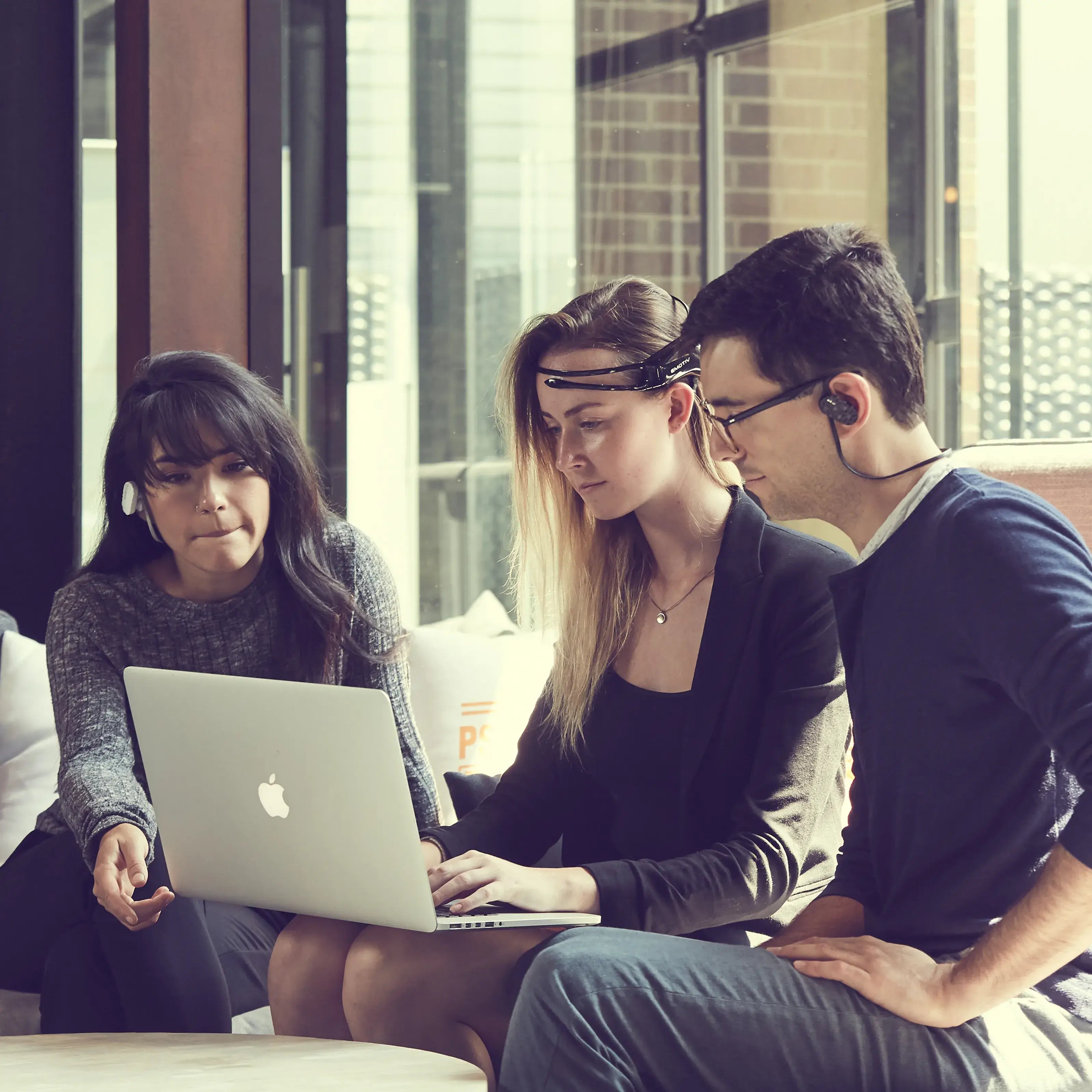 Three people in an office sitting in front of a laptop wearing Emotiv MN8 and Emotiv Insight