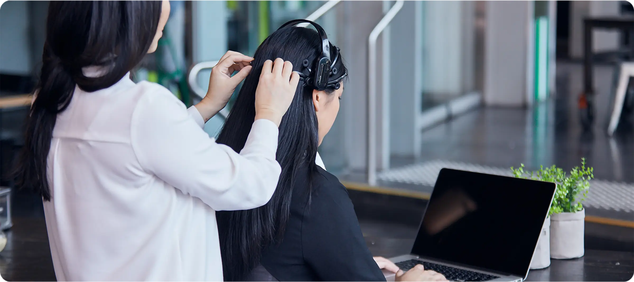 A researcher is setting up Emotiv Epoc X on a participant's head. The participant is sitting in front of an open laptop